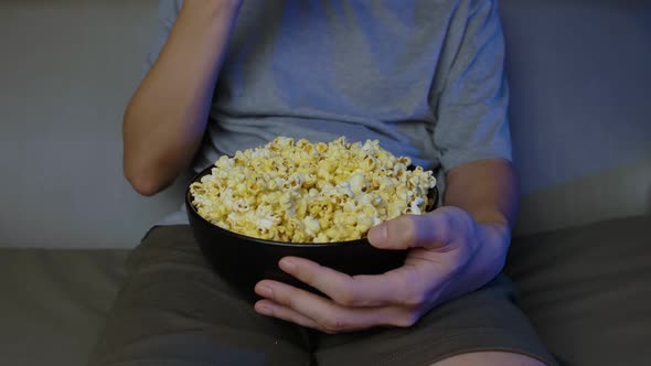 Close up, A man watching a movie and eating popcorn on the sofa at home. alt
