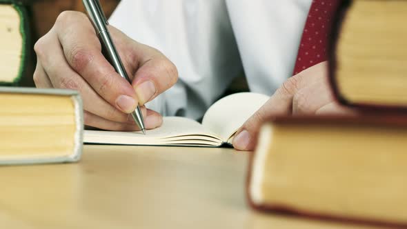 Closeup of Hands Writing in a Notebook at the Table with Books