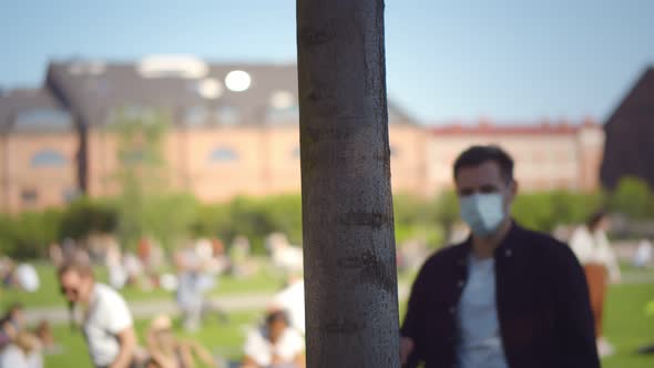 Couple of Young People Outdoors Putting Off Safety Mask and Hugging Tree Trunk with Eyes Closed alt