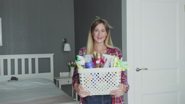 Woman with Basket Full of Sponges and Household Chemicals Look at Camera