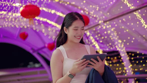 at night,young Asian woman happily plays with the tablet .She looks forward with hopes and dreams