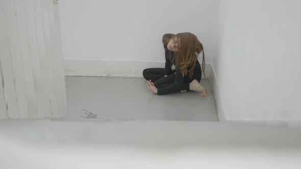 Young Woman Sits in Corner of Stairwell and Moves with Hair in Face alt