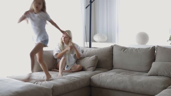 Little Girl Jumping on the Couch Next to Her Mom