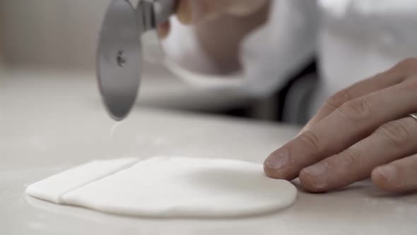 Closeup of Man Hands Using Pizza Cutter Wheel to Cut White Sugar Paste