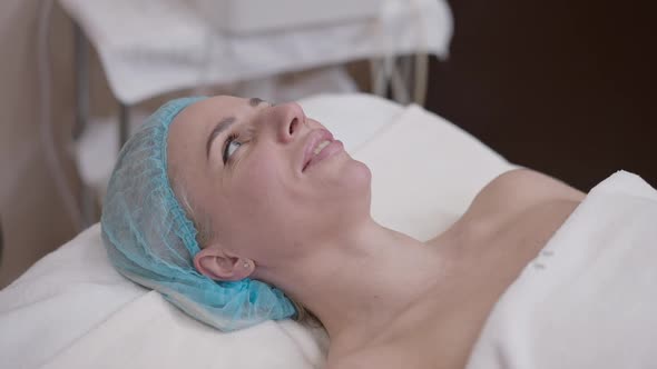 Confident Attractive Caucasian Woman in Shower Hat Lying in Spa Salon Talking Smiling in Slow Motion alt
