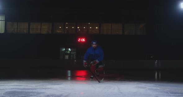 Man Hockey Player in Hockey Uniform Leaves with a Stick in His Hands Out of the Darkness and Looks alt
