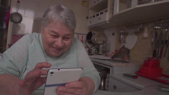 Senior Woman Holding Smartphone Laugh at Domestic Kitchen