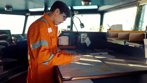 Filipino Deck Officer on Bridge of Vessel or Ship. He Is Plotting Position on Chart alt