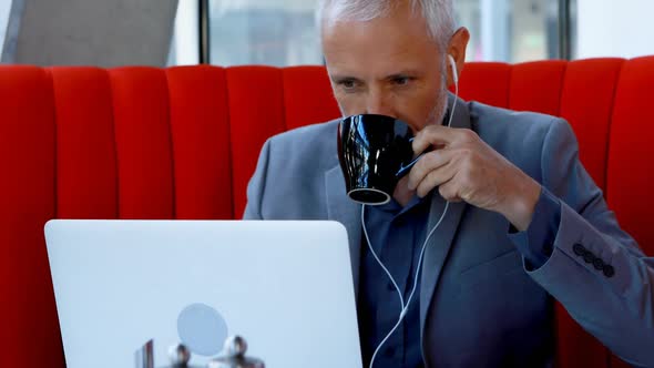 Businessman having coffee while using laptop in hotel 4 alt