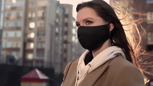 Nice Girl Brunette in Black Virus Mask Stands in the Wind alt