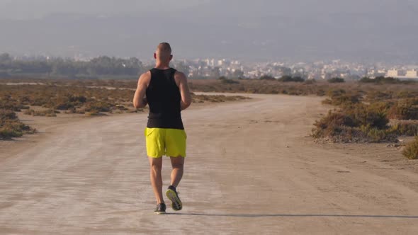 Muscular Sporty Man Jogging in Desert with City Background