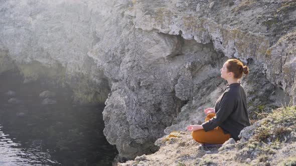 Positive Woman Meditates Sitting Rocky Coast Sunlight