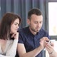 A Young Man and His Wife are Sitting on the Sofa in the Living Room and Looking at the Phone - VideoHive Item for Sale
