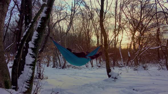 man lying in hammock under the trees in the winter forest alt