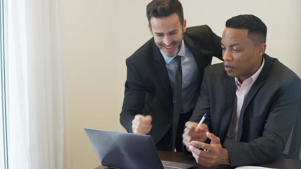 Businessman and colleague looking at document and laptop computer