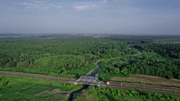Small River Flows Smoothly Between Green Fields and a Railway Bridge alt