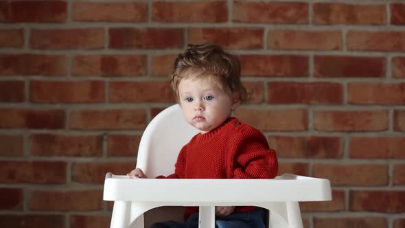 Toddler baby sitting in armchair. Brick wall on background.