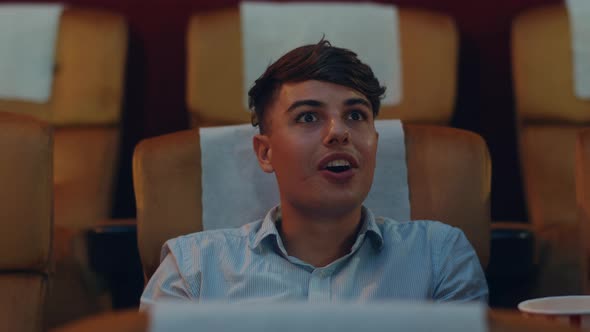 Attractive cheerful young caucasian man laughing while watching film in movie theater. alt