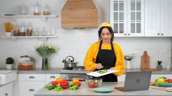 Woman in Kitchen Knives Sliced Cucumber From Cutting Board Into Glass Salad Bowl alt
