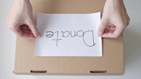 Hands Glues Sheet with Inscription Donate on Donation Box Top View alt