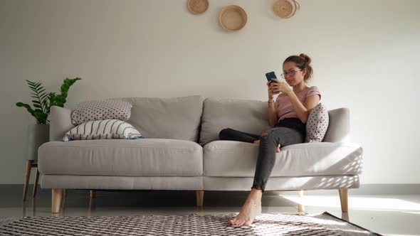 Young Woman Get Angry While Using Smart Phone Texting Messages Sitting on Sofa alt