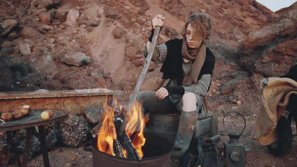 Dystopian Woman Sitting by Campfire in Garbage Can alt