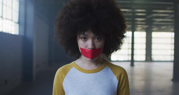 Portrait of african american woman with red tape on her mouth in empty parking garage alt