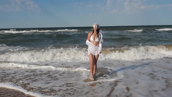 Brunette Woman in a White Swimsuit Stand Along a Sandy Beach alt