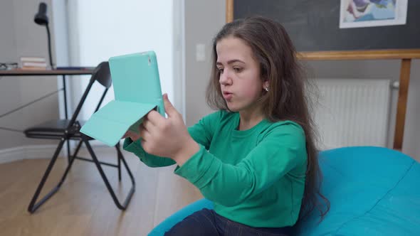 Medium Shot Portrait Positive Charming Little Person Sitting on Bag Chair Talking at Tablet Video alt