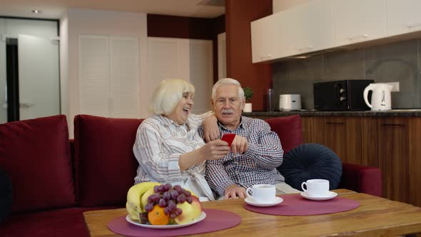 Senior Old Couple Grandparents Talking and Using Mobile Phone Computer at Home. Internet Shopping alt