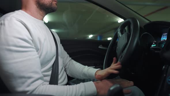Man Driving Car Through an Underground Parking Lot and is Looking for a Place to Park or Drives Away alt