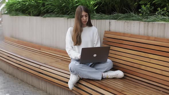 Young Female in Garden Using Laptop Communicates on Internet with Customer alt