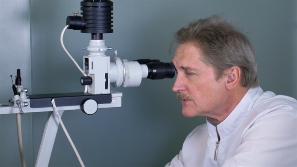 Attentive optometrist examining male patient on slit lamp