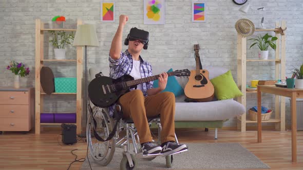 Young Man Disabled Musician in a Wheelchair and Virtual Reality Glasses Playing Guitar alt