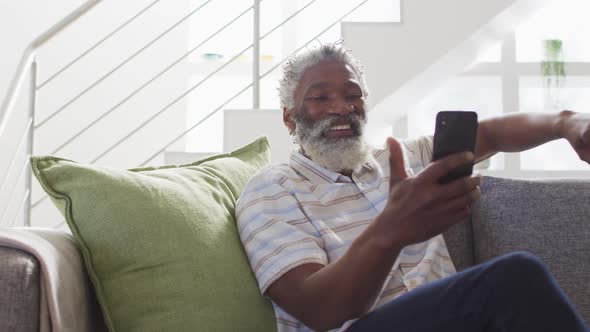 Senior man having a video chat on his smartphone at home alt