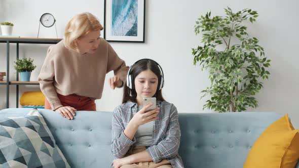 Offended Teenager Listening To Music and Using Smartphone Ignoring Angry Mother alt