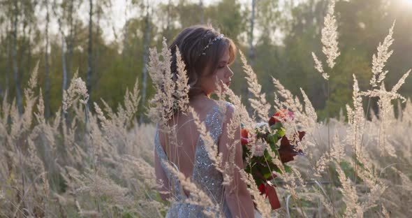 A Young Woman Dressed in a Gray Wedding Dress. She Has Flowers in Her Hand and Is in the Park alt