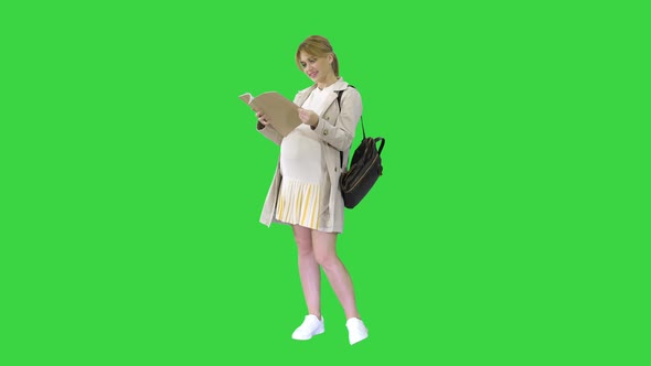 The Pregnant Woman Standing with a Book on a Green Screen, Chroma Key. alt