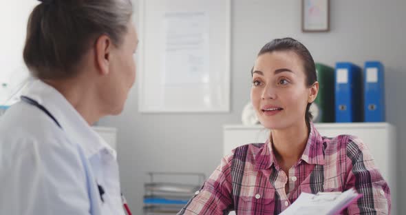 Happy Beautiful Young Woman Looking at Friendly Doctor During Visit in Hospital alt