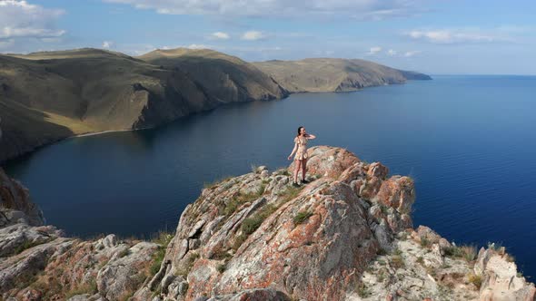 Young Woman in White Short Dress Running Up on Top of Mountain Above the Lake