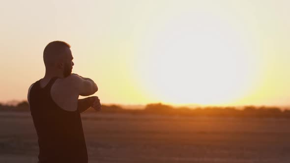 Sporty Man with Smartwatch Stretching Arms on Beach at Sunset alt