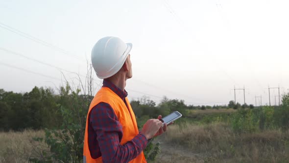 Engineer Inspects a Power Line Using Data From Electric Sensors on a Tablet.