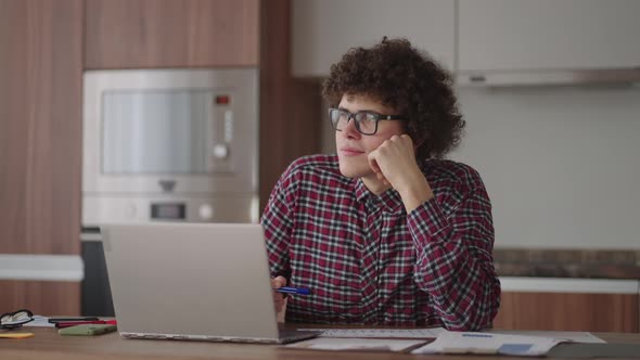 Curly Haired Male Student Attractive Young Boy in Glasses is Studying at Home Using Laptop Typing alt