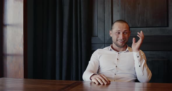 Exasperated Man Sitting at an Indoor Table Shaking His Head and Gesturing with His Hands Showing alt