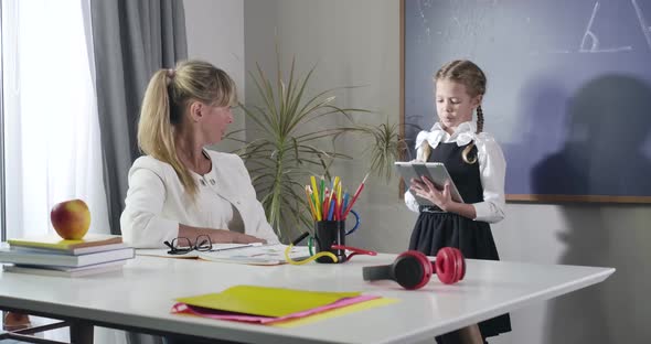 Charming Caucasian Girl in School Uniform Declaiming To Middle Aged Teacher Sitting at the Table alt