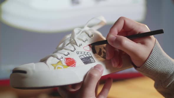 Male's Hands Putting Coloured Unique Patterns On Sneakers While Designing Shoe On A Desktop At Home alt