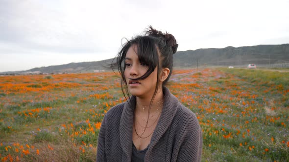 A beautiful young woman crying and looking emotional and sad in a field of wild flowers with wind bl alt