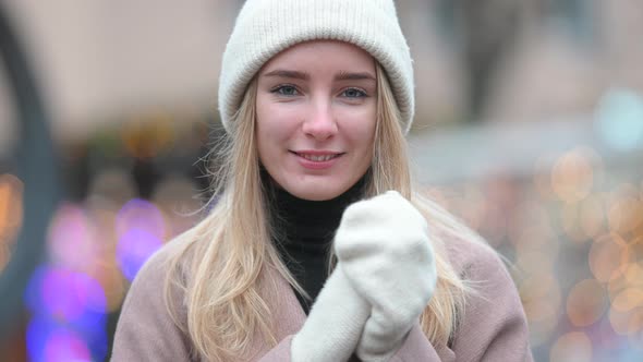 Portrait of a young girl in a polto hat and mittens against the background of festive lights