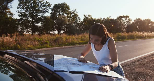Alone Woman Driver Studying Map on Car Hood, Planning Her Route at Countryside alt