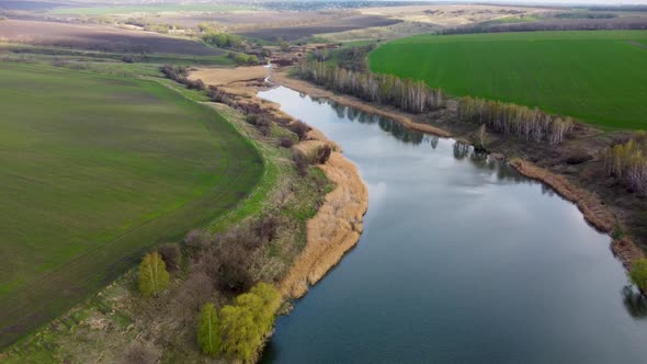 Fly up scenic lake with young green spring fields